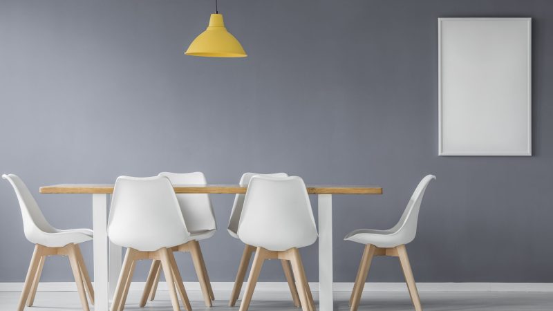 Mockup of poster in grey dining room interior with white chairs at wooden table under yellow lamp